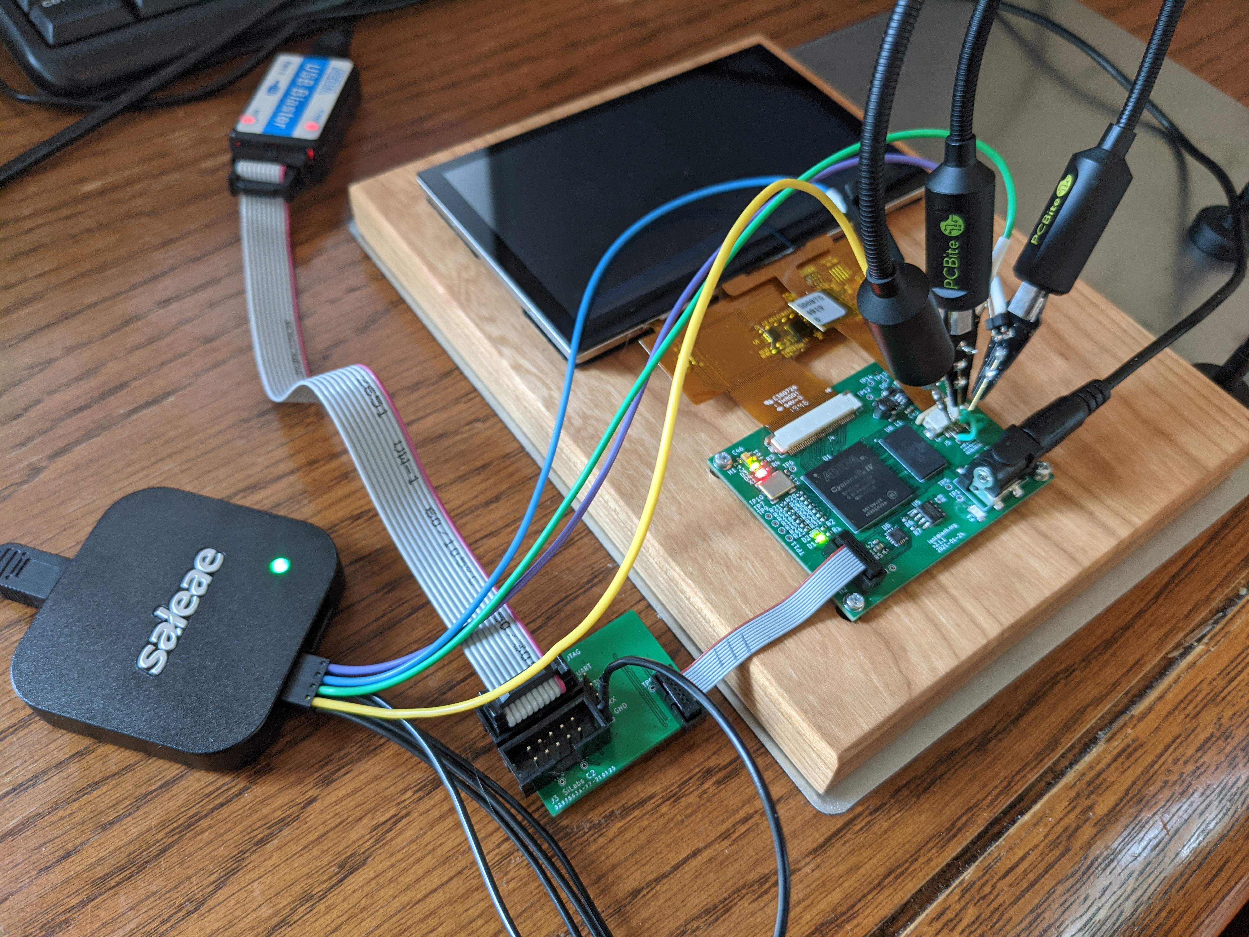 A picture of the board with a debug board attached to an altera programmer. There's also a USB logic analyzer connected to some hands-free probes, which are probing the touchscreen connector.